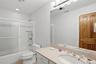 The bathroom features a vanity with a light-colored countertop and a mirror, and a shower-tub combination with sliding glass doors