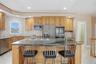 The kitchen features wood cabinetry, stainless steel appliances, a large island with a cooktop and seating, granite countertops, and a tiled backsplas