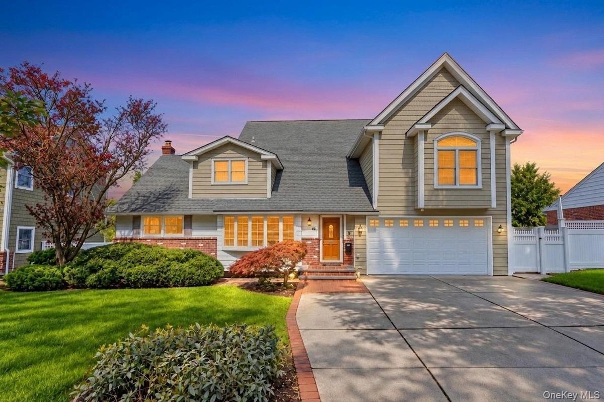 Traditional-style home featuring a two-car garage, brick paver walkway, dormer windows, and a white picket fence