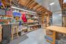 Utility space with exposed wood ceiling beams, overhead lighting, concrete flooring, and extensive metal shelving