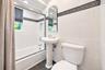 White tile walls featuring a decorative border, pedestal sink, and a built-in bathtub with a glass enclosure
