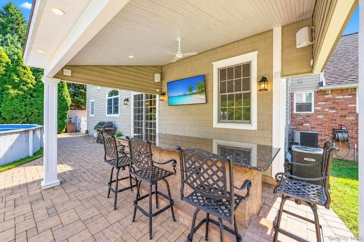 Covered outdoor patio featuring recessed lighting, a ceiling fan, and a built-in bar with a dark stone countertop