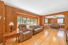 Hardwood flooring throughout, wood-paneled walls, a bay window with natural light, and a ceiling fan in the recessed area