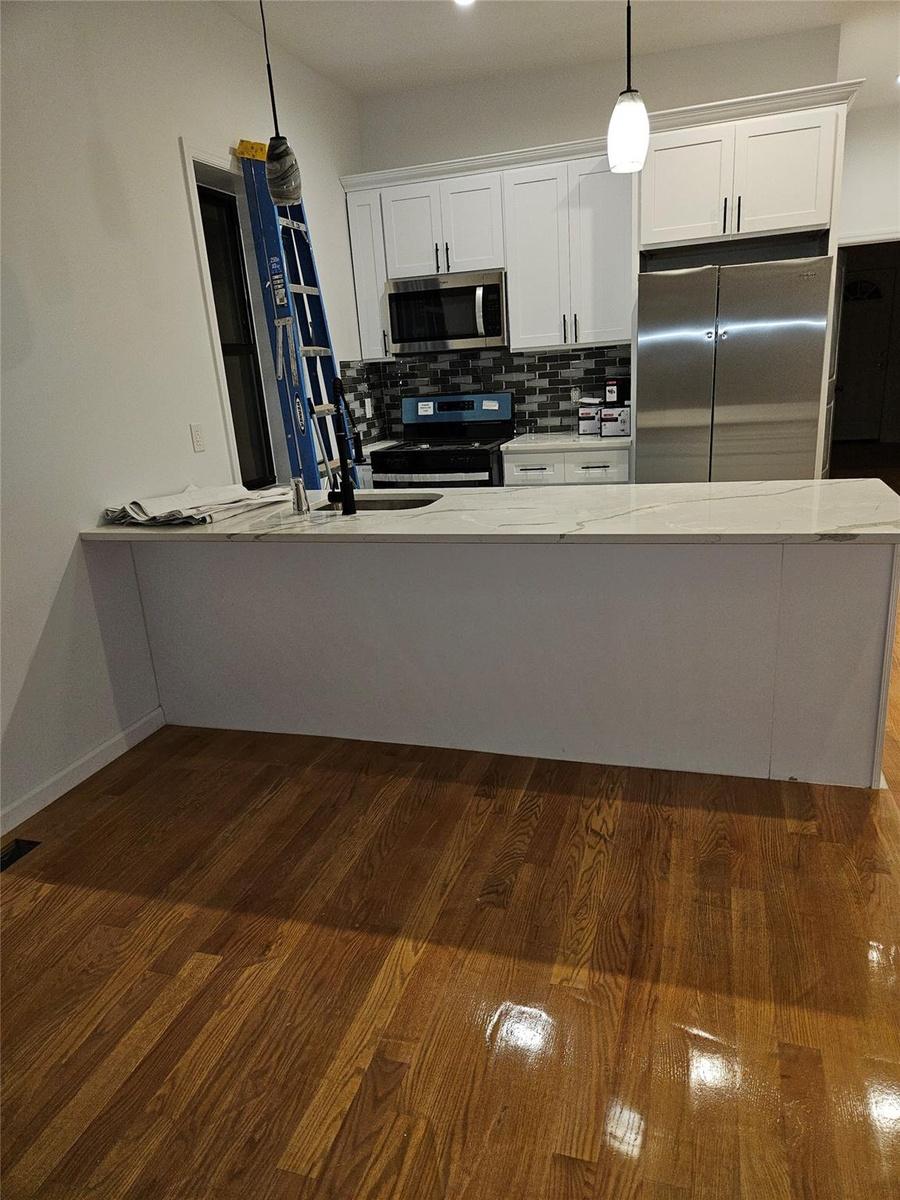 Kitchen with dark wood finished floors, a sink, decorative backsplash, appliances with stainless steel finishes, and white cabinetry
