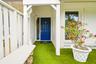 Covered entry with a vibrant blue door, white lattice wall accents, bright green artificial turf, and a white picket fence