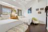 Vaulted ceiling with exposed beams, wood-finish flooring, two large windows with woven blinds, and an integrated ceiling fan