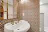 Pedestal sink with brass hardware, framed mirror, patterned wallpaper, and a glass-enclosed shower with tiled walls