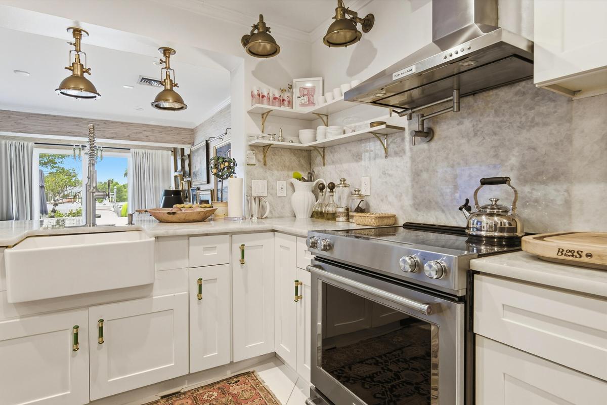 White shaker cabinetry, farmhouse sink, stainless steel range, stainless steel range hood, and light-toned countertops
