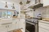 White shaker cabinetry, farmhouse sink, stainless steel range, stainless steel range hood, and light-toned countertops