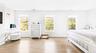 Light wood-finish flooring, three windows with white frames, white walls, and an upholstered bed frame