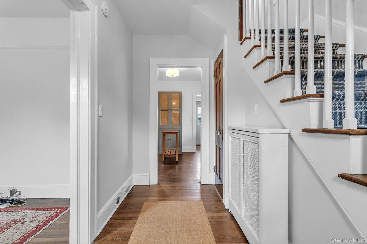 Hardwood flooring, painted white baseboards, a staircase with white balusters and wood-finish treads, and a built-in radiator cover