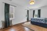 Hardwood flooring throughout, multiple windows with roller shades, cast iron radiator, and ceiling-mounted light fixture