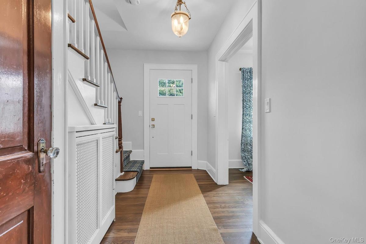 Hardwood flooring, white paneled door with glass inserts, staircase with white risers and wood treads, built-in radiator cover, and hanging light fixt