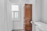 White subway tile walls, wood-finish storage cabinet, window with plantation shutters, white toilet, and gray floor tiles