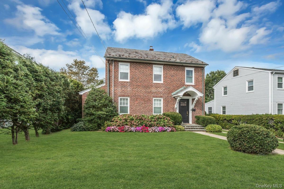 Brick exterior with a slate shingle roof, covered front entry, landscaped planting beds, and a concrete pathway