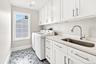 spacious Laundry Room with white shaker-style cabinetry with brushed nickel hardware, light-toned countertop, under mount stainless steel sink with go