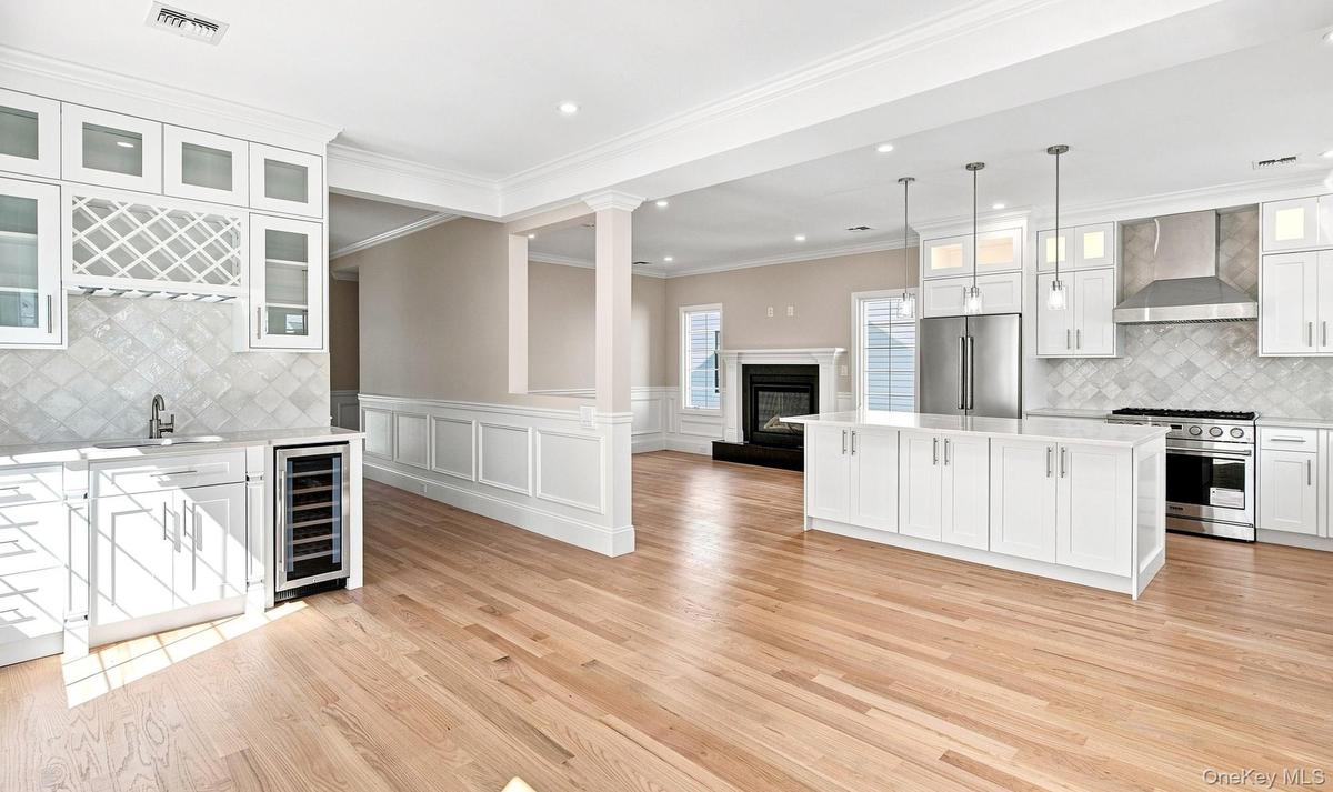 Great Room cross-view of kitchen, family room and dining. Light wood-finish flooring throughout, white cabinetry with glass-front uppers, stainless st