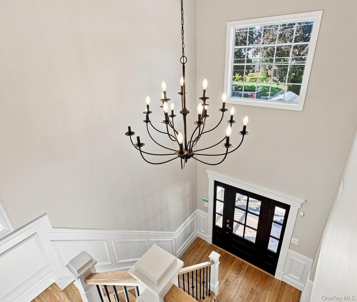 Spacious foyer featuring a multi-tier chandelier, wood-finish flooring, white panel molding, and a dark-toned entry door with multiple glass panes.