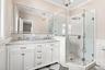 Dual vanity with under mount sinks, stone countertop, and an expansive mirror, large shower.