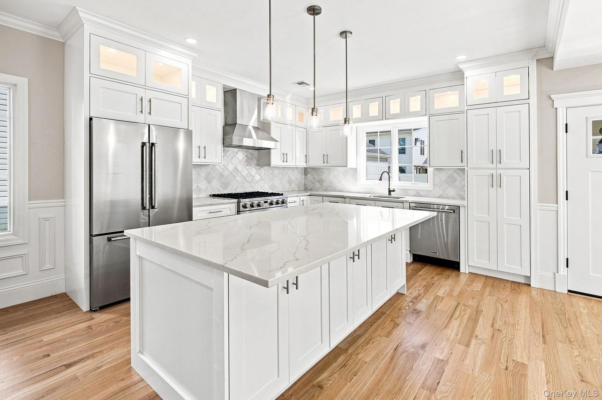 Gourmet Kitchen with a large center island featuring a white quartz countertop, stainless steel appliances, white shaker cabinetry, and wood-finish fl