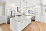 Gourmet Kitchen with a large center island featuring a white quartz countertop, stainless steel appliances, white shaker cabinetry, and wood-finish fl