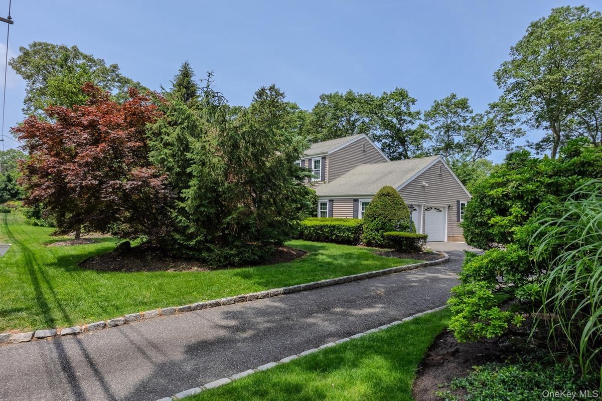 Asphalt driveway with stone border, two-car garage, and mature landscaping