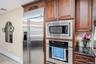 Stainless steel refrigerator, integrated microwave, built-in oven, wood cabinetry, and dark countertop