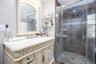 Vanity with an integrated sink, a large framed mirror, and a glass-enclosed shower with tile surround