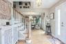 Hardwood flooring throughout, white painted staircase with wood handrail, traditional chandelier lighting, and a white entry door with decorative glas