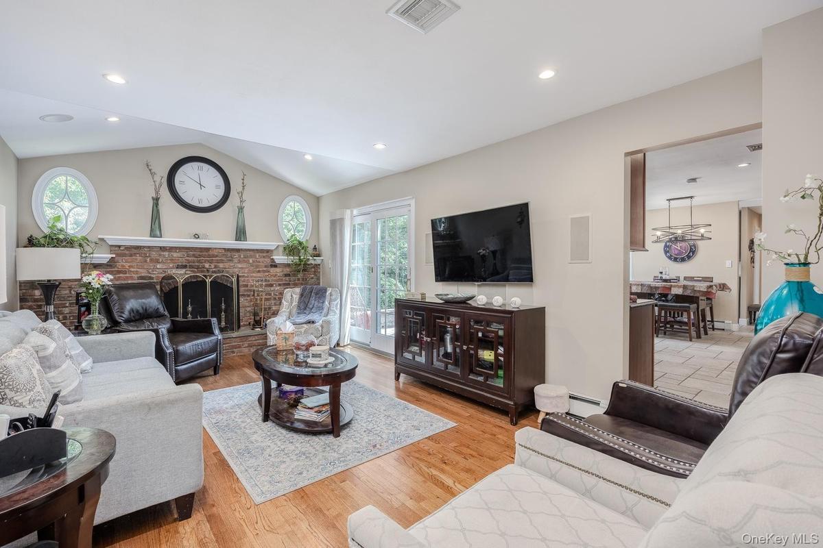 Vaulted ceiling, recessed lighting, brick-clad fireplace, wood-finish flooring, and French doors leading to exterior