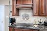 Integrated cooktop with a dark stone countertop, complemented by a decorative tile backsplash and custom wood cabinetry