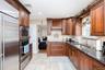 Warm wood cabinetry with crown molding, stainless steel appliances, dark stone countertops, tile backsplash, and a stainless steel sink with a goosene