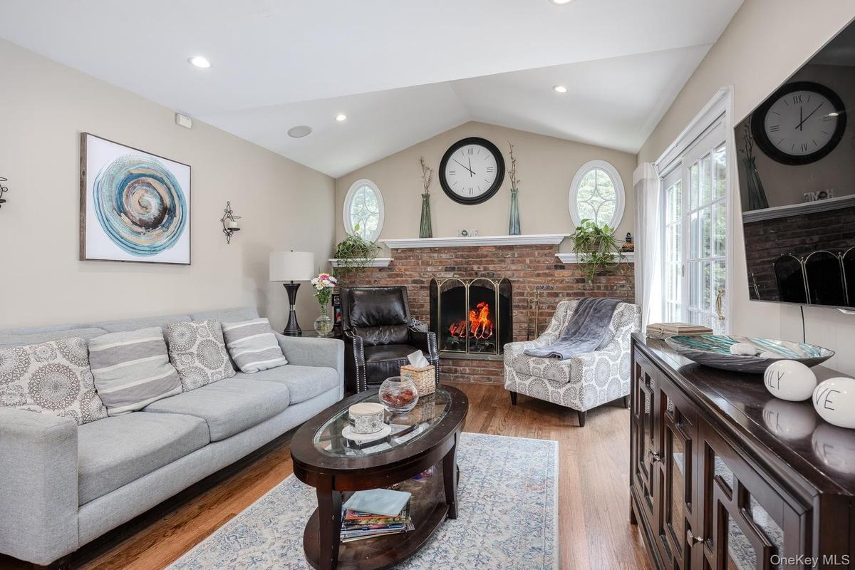 Vaulted ceiling living area featuring hardwood flooring, a brick fireplace, French doors, and recessed lighting