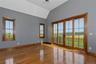 Hardwood flooring, vaulted ceiling, two windows with wood trim, and a four-panel sliding glass door with wood trim opening to a balcony with black rai