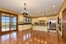 Wood-finish flooring, cream cabinetry, a central island with a dark countertop, stainless steel refrigerator, and double wall ovens