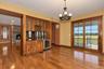 Wood-finish flooring, built-in cabinetry with glass doors, integrated beverage refrigerator, stone fireplace, and sliding glass doors to outdoor space