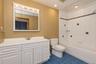 Built-in vanity with white cabinetry and integrated sink, mirrored medicine cabinet with vanity lighting, tiled shower and bathtub combination, and bl