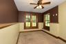 Carpeted room featuring multiple windows with wood trim, a ceiling fan with integrated lighting, and a partial wall with a wood cap