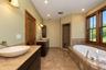 Dual vanity with vessel sinks and stone countertops, a built-in soaking tub, a tiled walk-in shower, and a large window with wood framing
