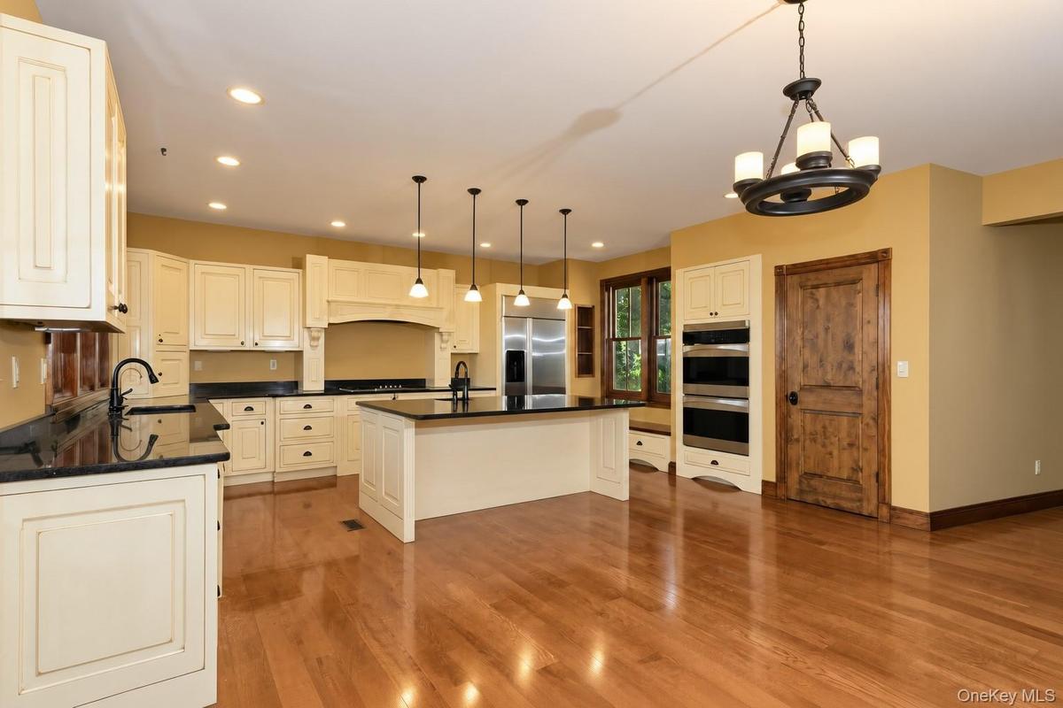 Kitchen featuring hardwood flooring, cream-finish cabinetry, dark countertops, a central island, and recessed lighting