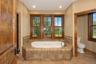 Soaking tub with tile surround, wood-framed windows, and recessed lighting