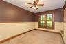 Dual-pane windows with wood trim, ceiling fan with integrated lighting, two-tone wall treatment, and carpeted flooring