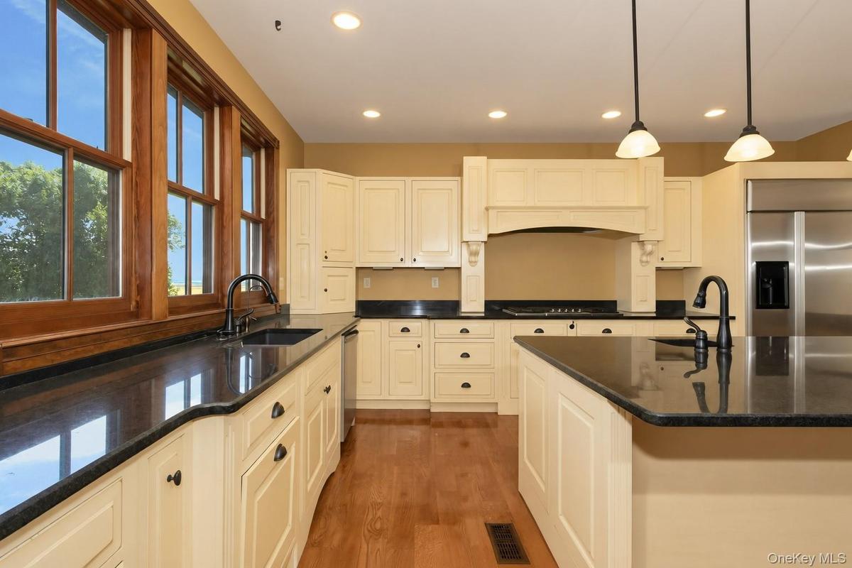Cream-colored cabinetry with dark hardware, dark countertops, wood-finish flooring, and recessed ceiling lighting