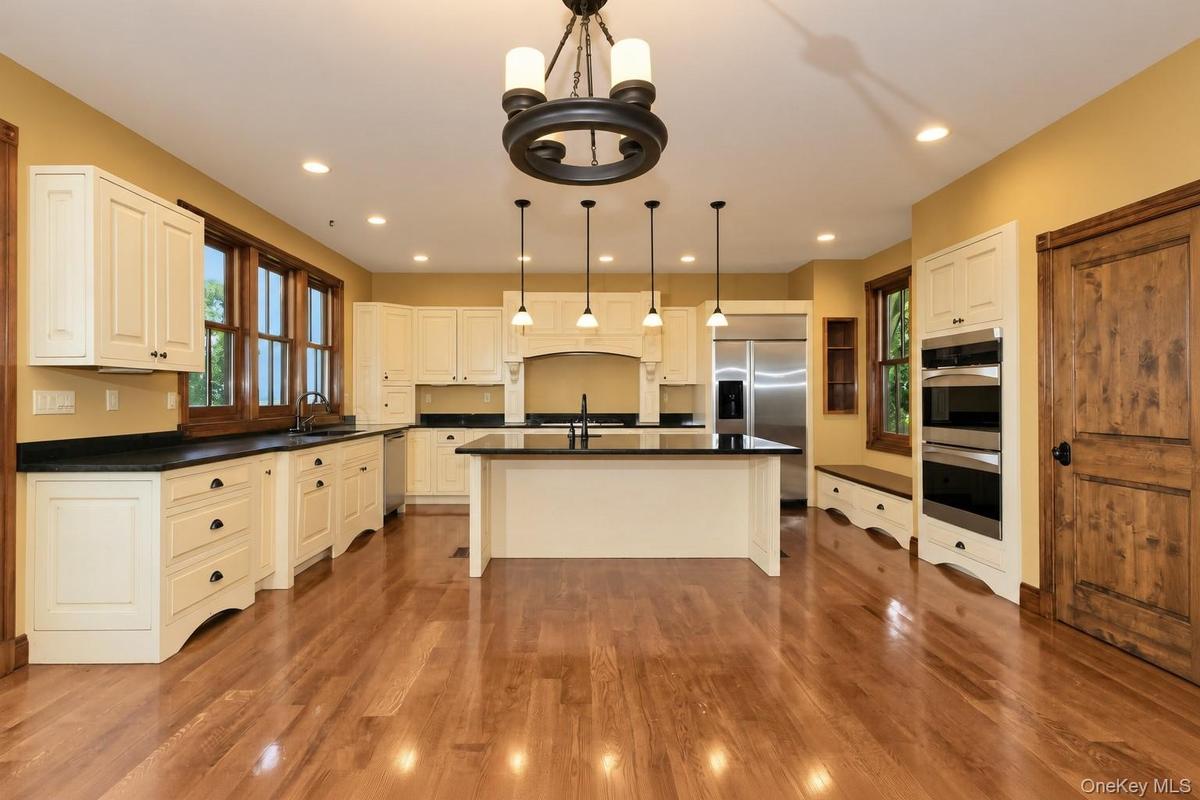 Hardwood flooring complementing cream cabinetry, a central island with countertop, recessed lighting, and stainless steel appliances
