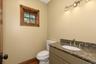 Vanity with a stone countertop and undermount sink, brushed nickel faucet, wall-mounted light fixture, and a window with wood trim