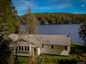 Lakefront property with mature trees, a shingled roof, and a prominent chimney