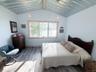 Vaulted metal ceiling with exposed wood beams, large window with wood trim, and wood-finish flooring