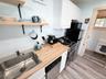 Compact kitchen featuring wood-finish countertops, a stainless steel sink, a dishwasher, a freestanding range, and upper cabinetry