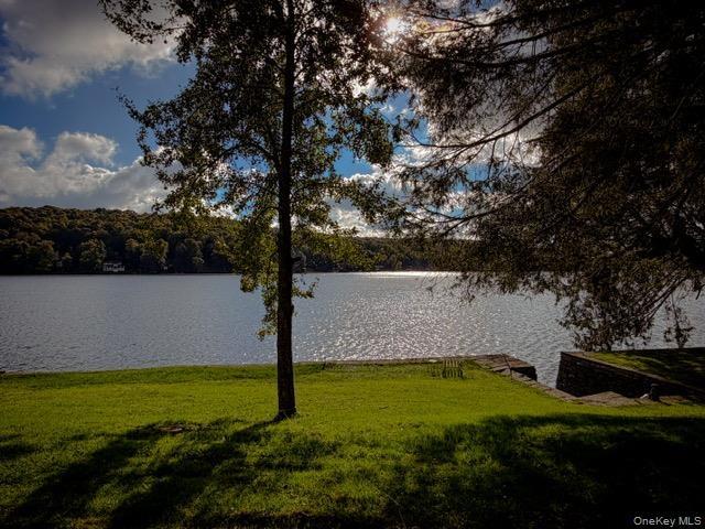 Expansive waterfront property featuring a manicured lawn, mature trees, and a stone retaining wall