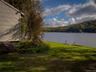 Lakeside property featuring a spacious lawn, mature trees, and a distant forested hillside
